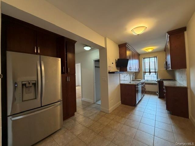 Modern kitchen featuring wood-finish cabinetry, stainless steel refrigerator, granite countertops, and tiled flooring