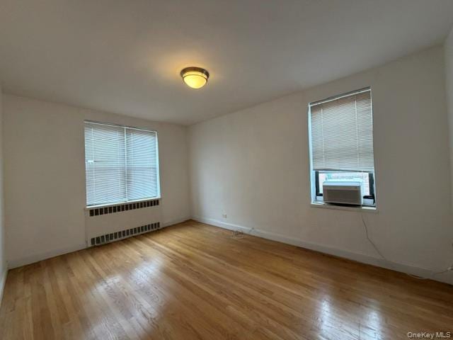 Hardwood flooring, two windows with blinds, wall-mounted heating unit, and an installed window air conditioning unit
